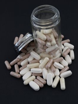 A spill of large white pills and brown capsules around a half filled bottle, over a black background.