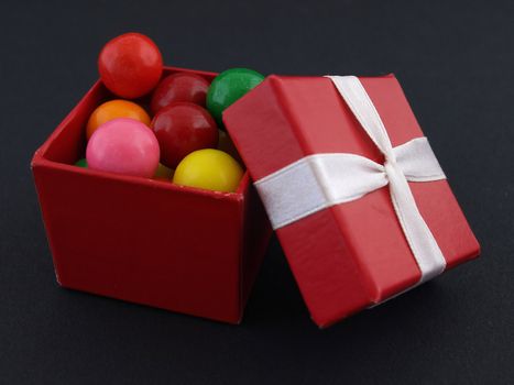Small red giftbox full of colorful gumballs. Isolated against a black background