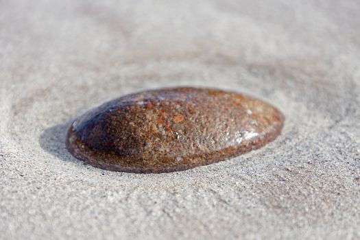 single red stone in sandy ground with water around