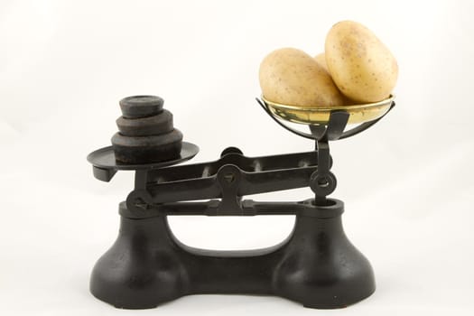 An old weighing scales painted black with a brass bowl containing potato tubers all isolated on white.