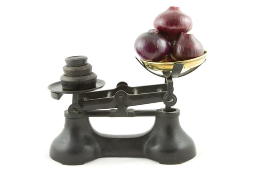 An old weighing scales painted black with a brass bowl containing red onions all isolated on white.