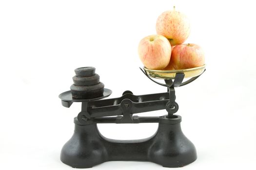 An old weighing scales painted black with a brass bowl containing apples all isolated on white.