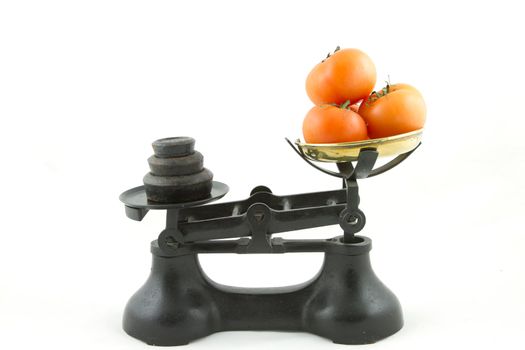 An old weighing scales painted black with a brass bowl containing tomatoes all isolated on white.