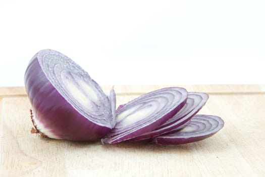 A red onion sliced on a wooden chopping board with a white background.