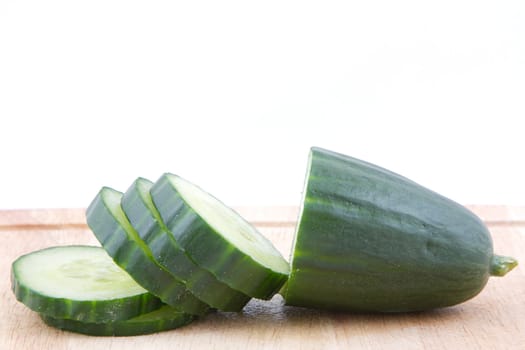 A sliced cucumber on a wooden chopping board with a white background.