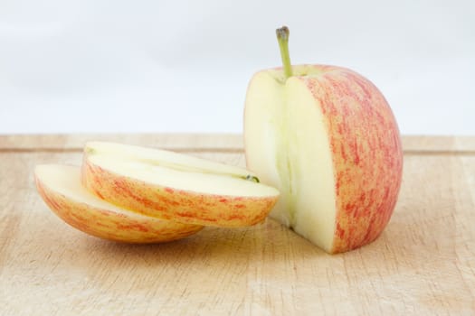 An apple sliced on a wooden chopping board with a white background.