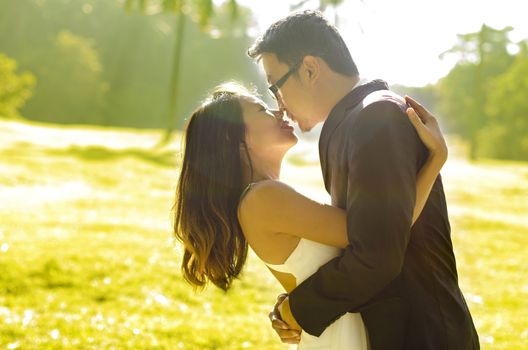 Bride and groom kissing in the park, back-lit in the morning.