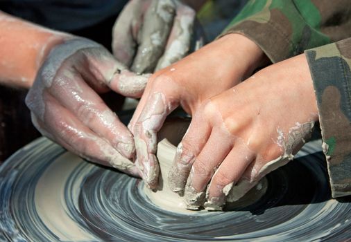 Potter hands guiding a child to create pottery