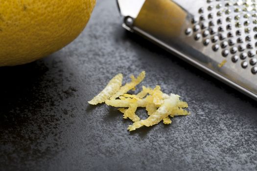 Lemon zest on black work surface with grater and lemon partially in frame.