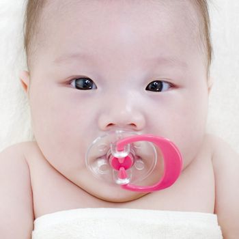Asian baby girl with a soother in her mouth lying on bed