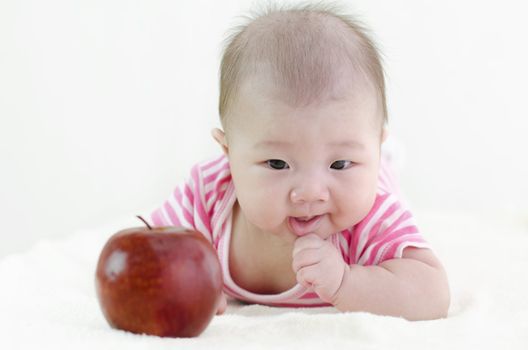 Asian baby girl trying to grab a large apple, focus on baby