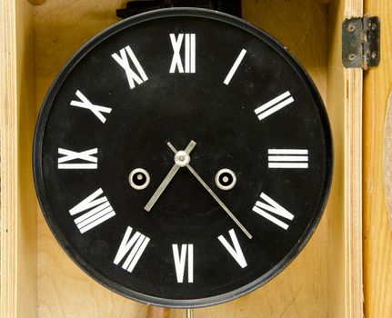 Ancient black clock with roman numbers and arrows. Antique clock in wooden box.