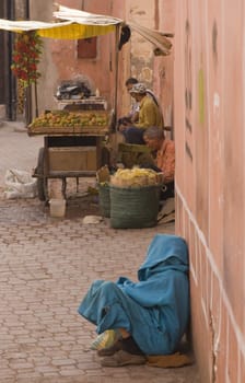 Cloaked figure squatting by a wall in an alleyway in the old city of Marrakesh, Morocco