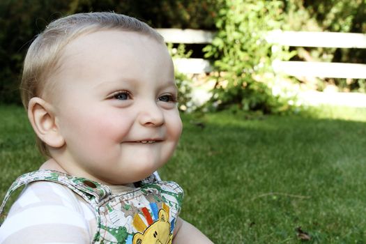 Cute blond baby boy sitting outside in the garden