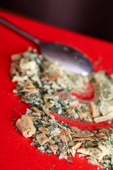 Herbs on a red surface with a silver spoon