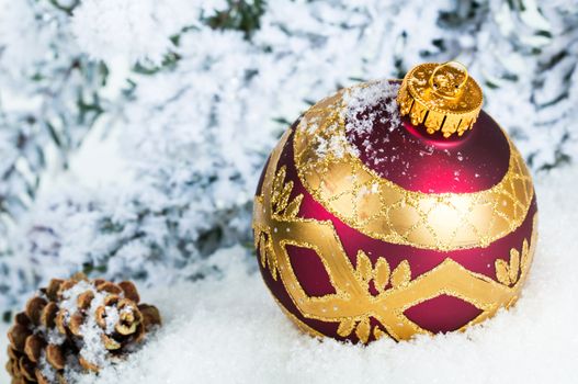 Close up of decorative Christmas ball on the snow and Christmas tree as a background.