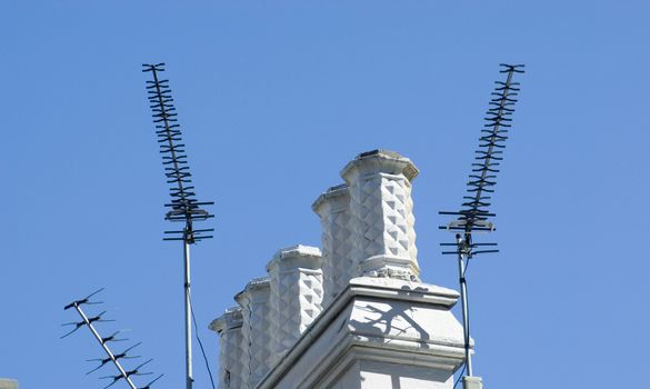 detail of a roof, chimney pot and aerials against a bue sky