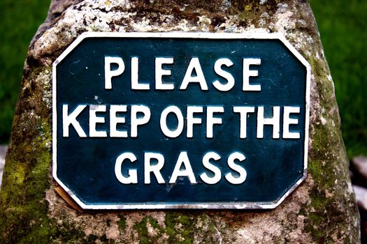 Please Keep Off The Grass sign mounted on a worn stone plinth and covered in moss