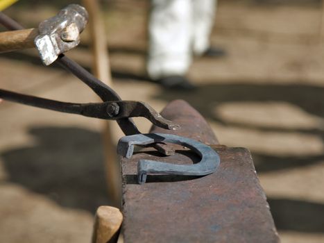 hands of blacksmith by working metal with hammer and anvil. Hammering glowing steel - to strike while the iron is hot.