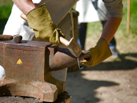 hands of blacksmith by working metal with hammer and anvil. Hammering glowing steel - to strike while the iron is hot.