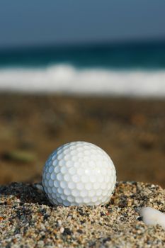 Golf ball on the beach ready to be hit in to the ocean.