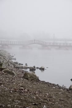 Foggy day on river's beach with view on bridge.