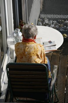 Retired female doing crossword puzzle at her balcony in the first spring sun.