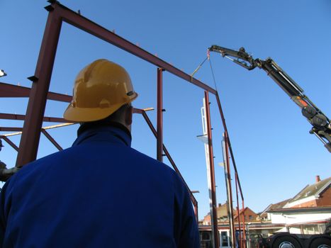 Construction worker overlooking  a crane working with some iron constructions.