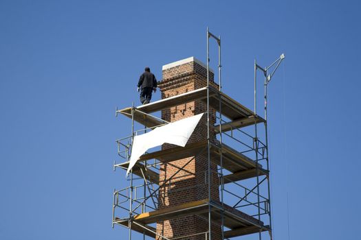 Man working on scaffold around renovated chimney.