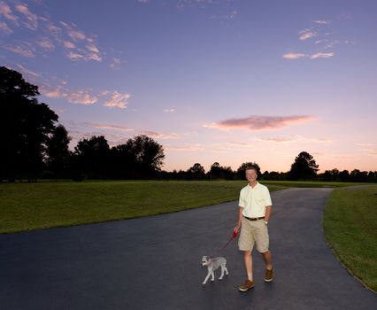 Senior man walking small puppy at dusk as the sun sets behind them