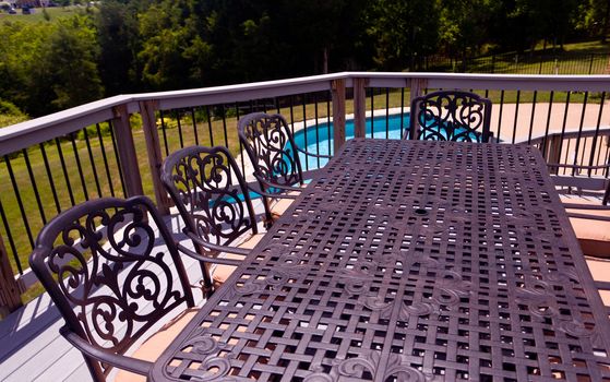 Modern table and chairs on wooden deck with swimming pool in back yard garden setting