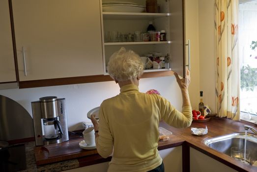 Elderly female standing in her kitchen making coffee.