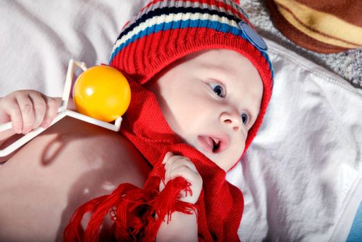 Bright portrait of beautiful baby in the red cap and scarf and with a toy in the hands.