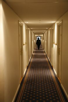 Black dressed person walking down a long hotel corridor. Motion blur.