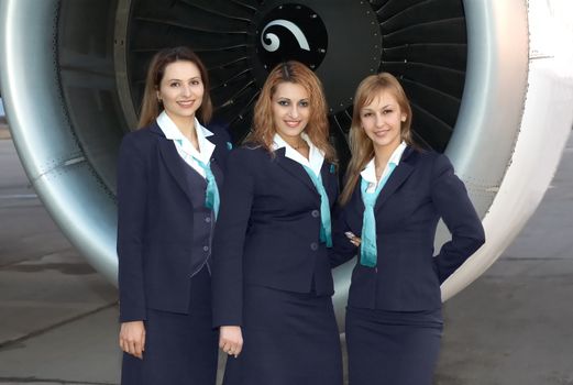 Three beautiful stewardesses in front of aircaft engine