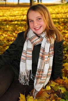 Portrait of a beautiful teenage girl in a fall park with fallen leaves