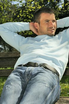 attractive man is relaxing on a bench in a natural environement