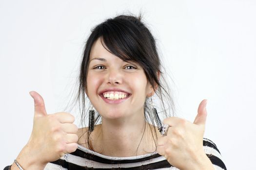 Funny candid shot of a young dark haired woman smiling and making the two thumbs up sign of approval, studio shot over white.