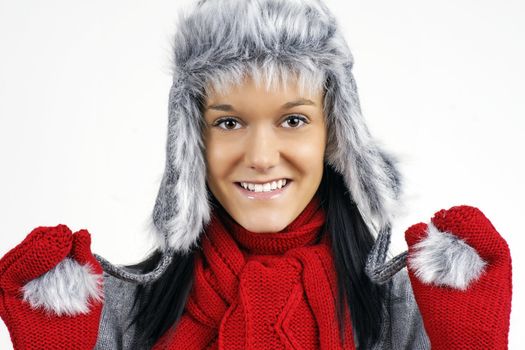 Fun smiling friendly young woman ready for the cold weather with her furry grey hat and red scarf and mittens.