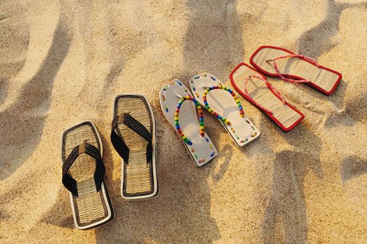 Three pair of beach sandals on the sandy beach