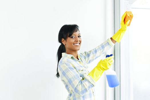 Smiling black woman cleaning windows with glass cleaner