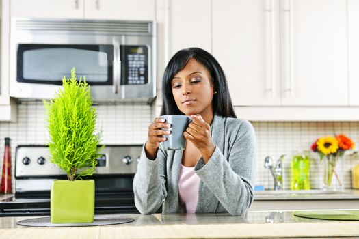 Thoughtful black woman holding coffee mug in modern kitchen interior