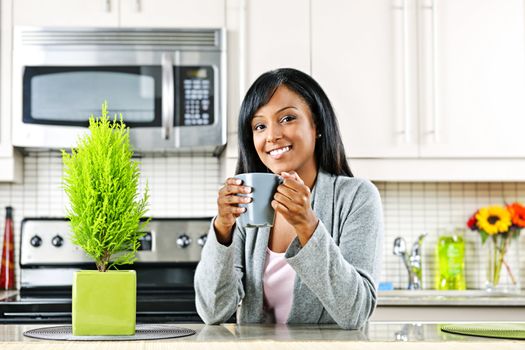 Smiling black woman holding coffee mug in modern kitchen interior