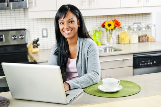 Smiling black woman using computer in modern kitchen interior