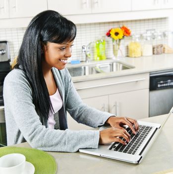 Smiling black woman using computer in modern kitchen interior