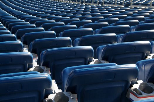 Red staduim seats cast in bright sunshine and shot from behind.
