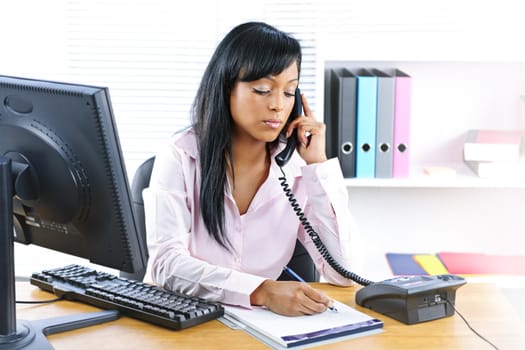 Serious young black business woman on phone taking notes in office