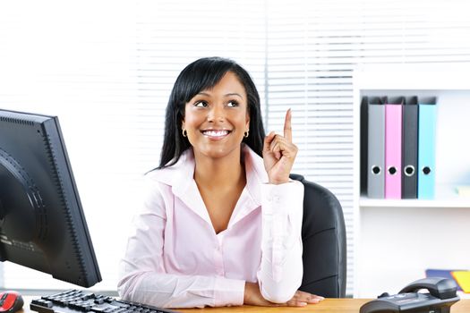 Smiling black business woman pointing up with idea at desk in office