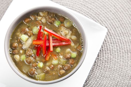 Bowl of fresh soup with kapucijners green onions and red bell pepper garnish