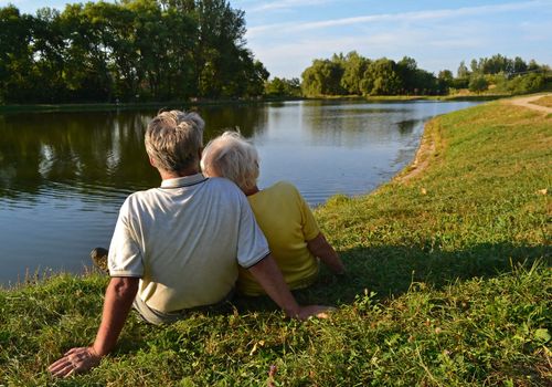 A senior couple sitting and relaxing together on a lakeside on a sunny afternoon.